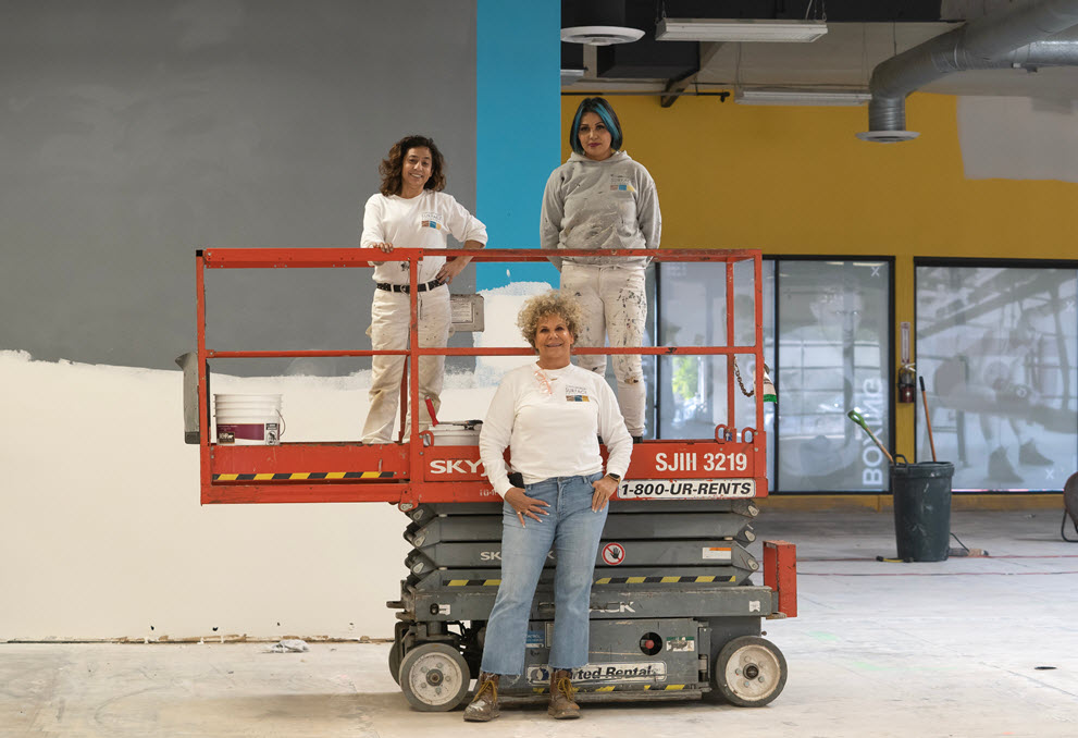 Image of a womans foot next to a 5 gallon can of Behr Premium Paint