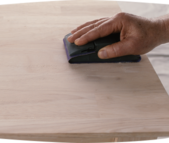 A person sanding a wooden table with a sanding block