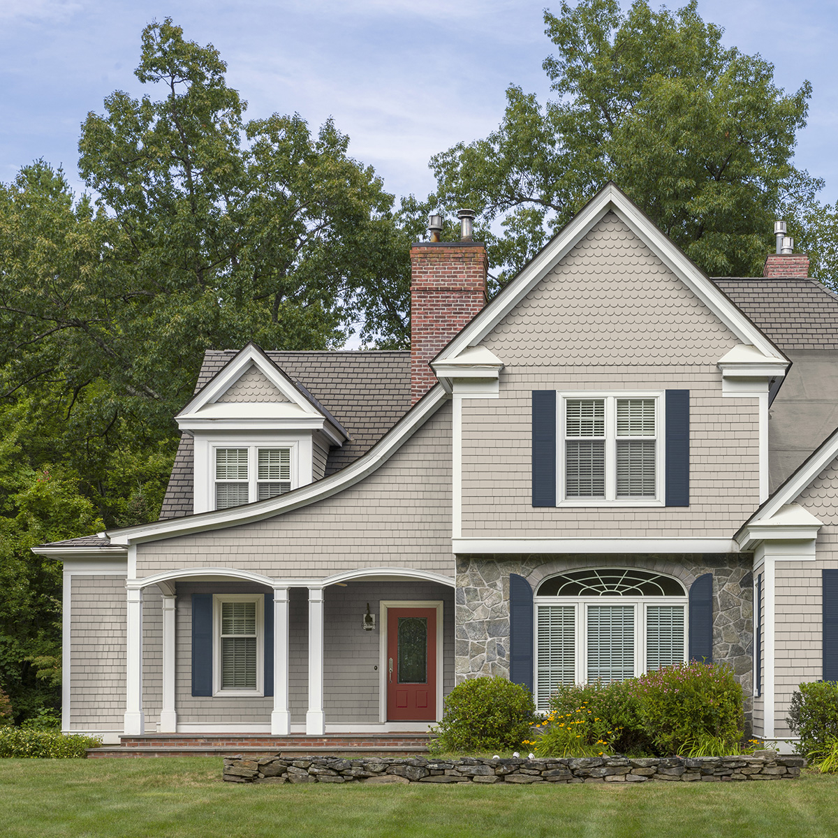 A neutral house exterior with blue shutters and a red door painted with Behr Dynasty Exterior paint
