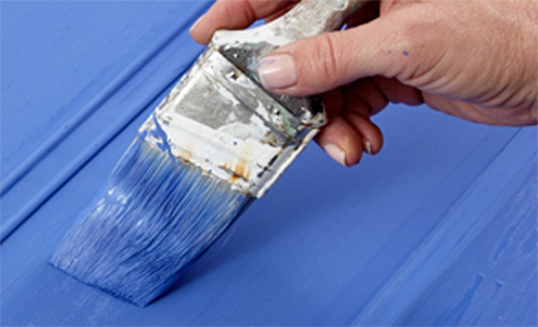 Person's hand with paint brush painting blue paint on the wall