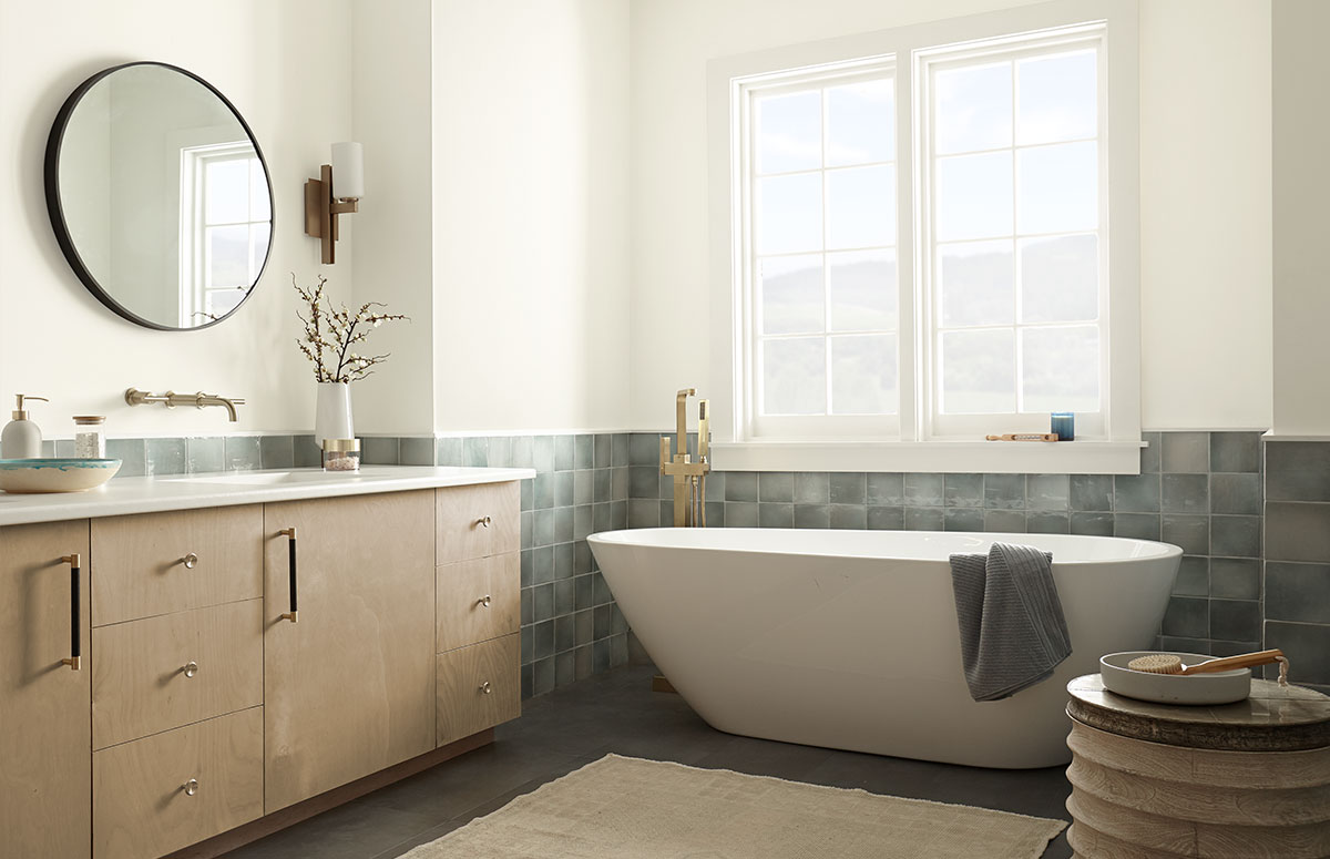 Serene bathroom highlighting off-white vs pure white tones, featuring Natural White walls, Ultra Pure White trim, a light wood vanity, gray tile surround, and a freestanding bathtub